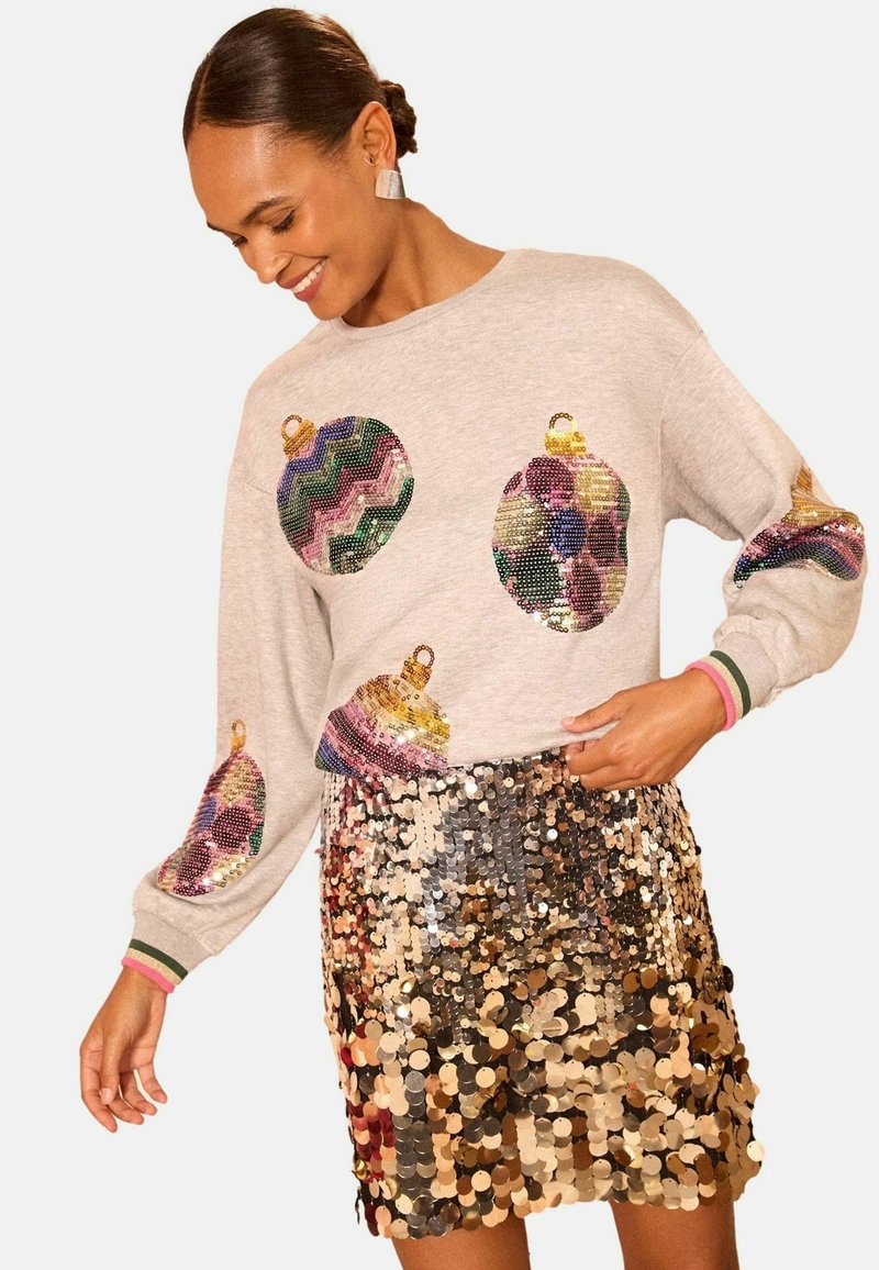 Sudadera gris con diseños ornamentales de lentejuelas coloridas, combinada con una falda brillante de lentejuelas en múltiples tonos, que muestra una vibrante textura y contraste.