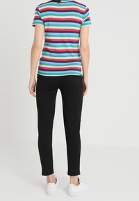 Gestreept T-shirt met korte mouwen in blauw, groen, rood en wit, gecombineerd met zwarte slim-fit broek en witte sneakers. Simpel, casual outfitontwerp.