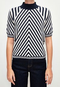 Triko s krátkým rukávem s námořnickými a bílými diagonálními pruhy, vysoce žebrovaným límcem a přiléhavým střihem, v kombinaci s tmavými džíny.