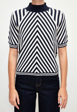 Top en tricot à manches courtes présentant des rayures diagonales bleu marine et blanches, un col côtelé haut et une coupe ajustée, associé à un jean foncé.