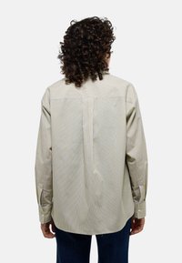 Chemise à boutons rayée dans des couleurs claires avec des rayures multicolores verticales, détail au dos et poignets boutonnés. Elle présente une coupe décontractée.