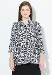 Schwarz-weiße gemusterte Bluse mit einem Schalkragen und dreiviertel Ärmeln, die geometrische Formen und abstrakte Designs aufweist.