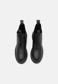 Czarne skórzane botki za kostkę z elastycznymi panelami bocznymi, uchwytami i teksturowanymi detalami. Posiadają grubą gumową podeszwę.