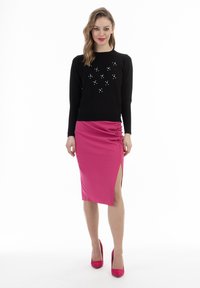 Maglione nero con un motivo decorativo e piccoli dettagli. Gonna rosa arricciata con spacchi laterali, abbinata a tacchi rosa coordinati.
