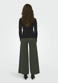 Top nero a costine a maniche lunghe abbinato a pantaloni svitati verde oliva, mostrato da dietro, con stivali neri con tacco.