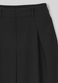 Pantalons noirs ajustés avec une coupe droite, dotés de plis avant, de poches latérales et d'une texture de tissu lisse. Design épuré et minimal.