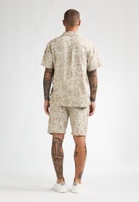 Short-sleeve beige shirt and matching shorts with intricate tan floral and paisley patterns. Casual fit with a relaxed texture.
