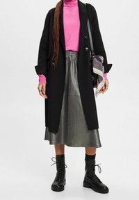 Zwarte wollen jas, roze coltrui, metallic zilveren midi-rok, zwarte veterschoenen, gestreepte sjaal, gelaagde texturen.