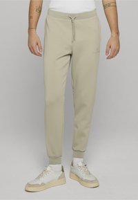 Světlé béžové tepláky z měkké látky s elastickým pasem a stahovacím provázkem. Mají zužující se střih a žebrované lemy.