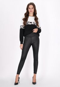 Fekete-fehér pulóver leopárdmintás zenekarral, fényes fekete leggings-szel és fekete tűsarkú cipővel párosítva. Sima textúra, testhezálló dizájn.