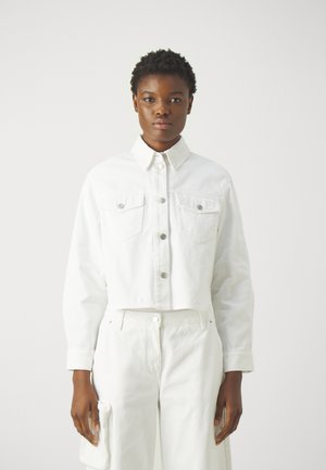 Giacca di jeans bianca cropped con due tasche sul petto, chiusura con bottoni e maniche lunghe. Abbinata a pantaloni di jeans bianchi a vita alta.