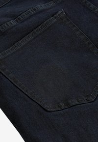 Jeans de mezclilla oscura con un solo bolsillo trasero, con costuras visibles y una textura suave. La tela está ligeramente desgastada.