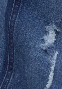 Mörkblå denimtyg med en sliten lapp som visar fransade kanter och ett ljusblått undertyg. Har en synlig sid söm och en grov väv.