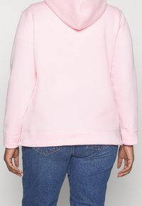 Vaaleanpunainen huppari, jossa on pehmeä kangas, suuri huppu ja resorivarsit. Yhdistetty sinisiin farkkuihin, joissa rento istuvuus.