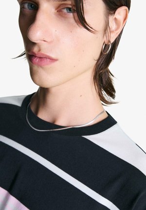 Maglietta a righe nere e grigie con scollo rotondo, accompagnata da una collana d'argento e orecchini a cerchio, indossata da una persona con capelli lunghi.