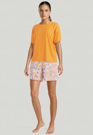 Top arancione a maniche corte abbinato a pantaloni corti con stampa floreale nei toni di rosa, giallo e bianco, con texture liscia e vestibilità rilassata.