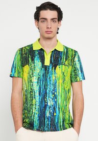 Polo skjorte med et livligt abstrakt design med grønne og blå striber, gule accenter og en ensfarvet limegrøn krave. Korte ærmer.