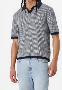 Polo de manga corta en un patrón de zigzag en azul marino y blanco, con un cuello y puños de contraste en azul marino, con un corte relajado y tejido texturizado.