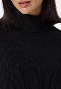 Schwarzer, gerippter Rollkragenpullover mit einem strukturierten Strickmuster und einem hohen Kragen. Der Stoff wirkt weich und warm.