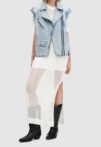 Denimväst med råa kanter, lager på lager över en vit stickad meshklänning med sidoklipp, matchat med svarta cowboystövlar.