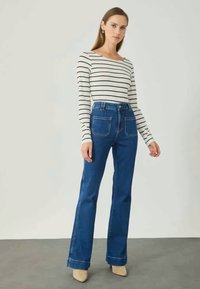 Blauwe denim flared jeans met achterzakken, gecombineerd met een wit-zwart gestreept shirt met lange mouwen. Heeft een klassiek ontwerp en een casual pasvorm.