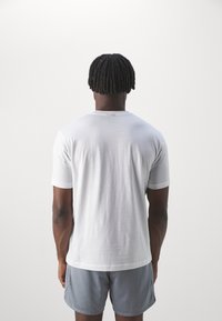 Camiseta blanca de algodón con mangas cortas y escote redondeado, combinada con pantalones cortos gris claro. Diseño sencillo, textura suave y sin patrones visibles.