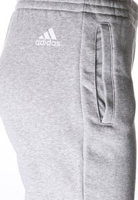 Graue Jogginghose aus weichem Material, mit einer Seitenasche und dem weißen Adidas-Logo. Elastischer Bund für eine enge Passform.