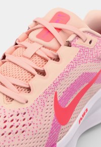 Lichtroze sneaker met een mesh bovenwerk, roze accenten en een levendige roze Nike swoosh-logo. Beschikt over een gestructureerde zool en een vetersluiting.