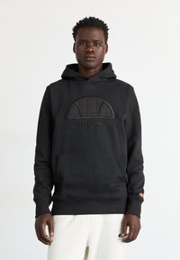 Sudadera negra con capucha y bolsillo frontal tipo canguro, que presenta un diseño de acento acolchado y texto de logo. Confeccionada en una tela suave.
