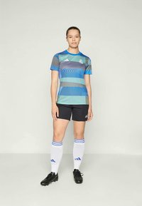 Modrá a tyrkysová pruhovaná futbalová dres s krátkymi rukávmi, čierne šortky, biele ponožky s modrými pruhmi a čierne kopačky. Viditeľné logo Adidas.