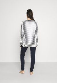 Top cu mânecă lungă, cu dungi alb-negru, cu decolteu rotund; combinat cu pantaloni tapered, de culoare albastru închis. Material moale, design lejer.