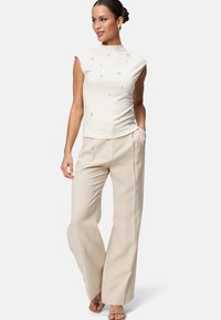 Haut sans manches blanc avec des petites embellissements, associé à un pantalon large beige. Tissu lisse et coupe ajustée. Sandales plates.