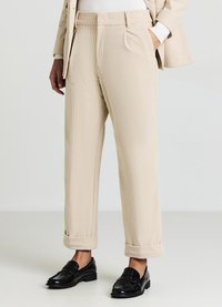 Beige Cordhosen mit lockerer Passform, einer vorgefalzten Vorderseite, Seitentaschen und umgeschlagenen Bündchen, kombiniert mit schwarzen glänzenden Slippern.