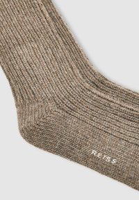 Braune gerippte Socke aus strukturiertem Material, mit verstärkter Zehen- und Fersenpartie. Weißes Logo "REISS" in der Nähe des Saums angebracht.