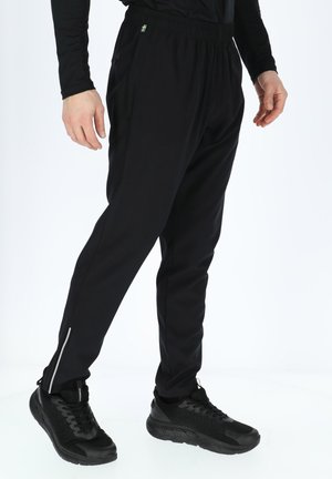 Black athletic pants made of stretchy material, with an elastic waistband, side pockets, and reflective zippers at the ankles.