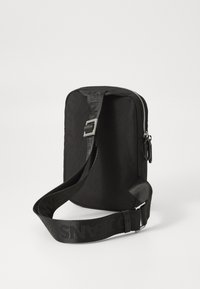 Borsa a spalla nera con forma rettangolare, realizzata in tessuto texturizzato, dotata di chiusura con zip, tracolla regolabile e dettagli con marchio.