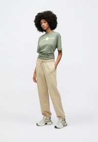 Πράσινη βαμβακερή μπλούζα με γραφικό "NIKE SHOX", μπεζ φόρμα με κορδόνι στη μέση και γκρι αθλητικά παπούτσια με μαύρες λεπτομέρειες.