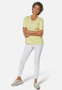 Gelbes T-Shirt mit kurzen Ärmeln und Rundhalsausschnitt, kombiniert mit weißen engen Hosen und beigen Schnürsneakern. Schlichtes Design, lässiger Look.