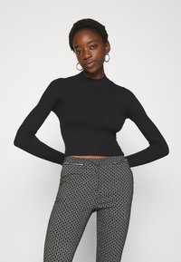 Haut court à manches longues noir côtelé avec un col montant, associé à un pantalon ajusté à motif noir et blanc avec un détail de zip.