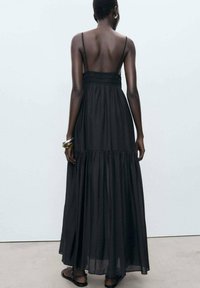 Robe maxi noire avec des bretelles spaghetti, un corsage froncé et une jupe à plusieurs niveaux. Tissu léger avec un design fluide et une texture transparente.