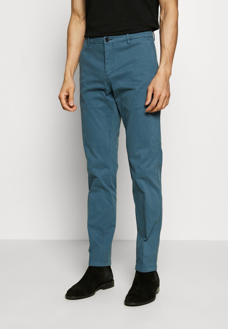 Pantalones de mezcla de algodón de color azul claro con un corte slim, bolsillos delanteros y cierre de botón, combinados con botas negras hasta el tobillo.