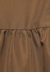 Hnědá látka s nabranými švy, vytvářejícími jemné faldy a strukturu textilního materiálu.