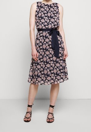 Blomstret kjole med navyblå baggrund, ærmeløs design og bælte bundet omkring taljen. Har en knælængde fald og blødt, let stof.