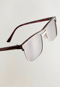 Brązowe okulary przeciwsłoneczne w kolorze tortoise shell o prostokątnym kształcie, z metalicznymi srebrnymi akcentami na ramie oraz szarymi soczewkami. Teksturowane zauszniki o błyszczącym wykończeniu.