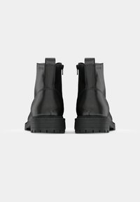 Botines de cuero negro con un acabado suave, forma redondeada, cremalleras laterales y suelas de goma texturizada para mayor tracción.