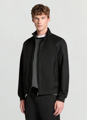 Blouson aviateur noir en tissu lisse, doté d'un col montant, d'une fermeture éclair frontale et de poches latérales, porté par-dessus une chemise à rayures.