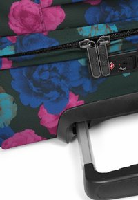 Blommig handbagageväska med en mörkgrön tyg som har rosa och blå blommor, dubbla dragkedjor och ett utdragbart svart handtag.