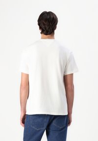 Hvid bomulds t-shirt med korte ærmer, rund halsudskæring og et enkelt design. Båret med blå denim jeans, der viser en afslappet pasform.