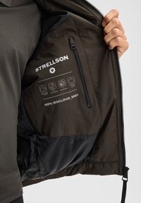 Dunkelolivene Jackeninnenseite mit Stofftags, die 100% ISOCLOUD_500®, leichtes Reisen und wetterfeste Eigenschaften detailliert beschreiben.