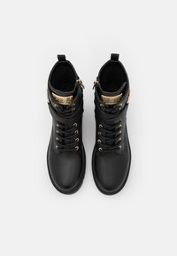Bottines en cuir noir avec une finition texturée, accents en métal doré, design à lacets et fermeture éclair latérale pour un enfilage facile.